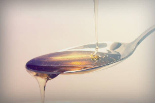 Honey pouring from spoon against a light background stock photo