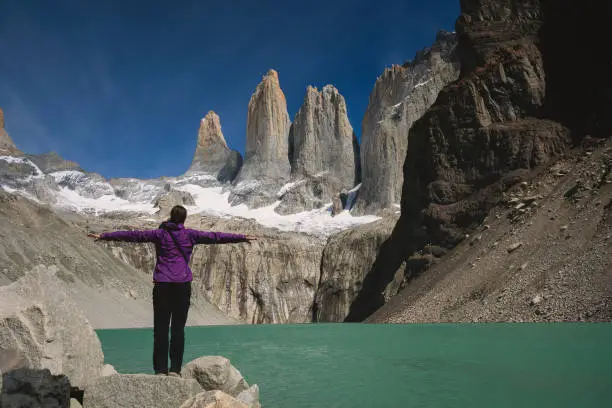 Young women is embracing amazing view of Torres del Paine towers with open arms in Patagonia, Chile.