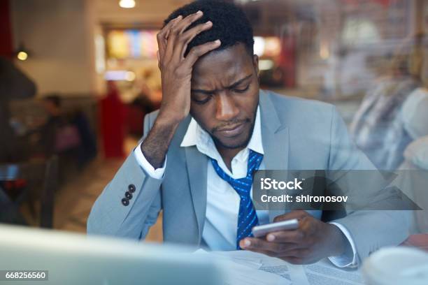Upset African Businessman With Smartphone In Coffee Shop Stock Photo - Download Image Now