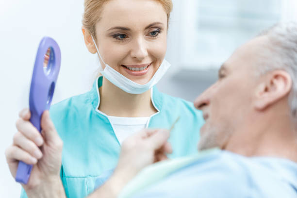 鏡を持ち、クリニックで成熟した患者を見て笑顔のプロの歯科医 - dental light dental equipment hospital professional occupation ストックフォトと画像