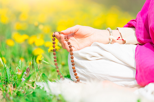 Recitation of mantras with mala hand during a practice yoga on a flowery meadow in spring