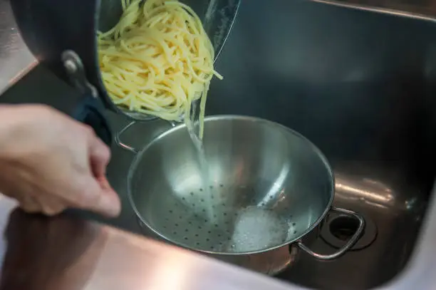 pot with spaghetti during the operation of the water draining cooking salt in the kitchen sink