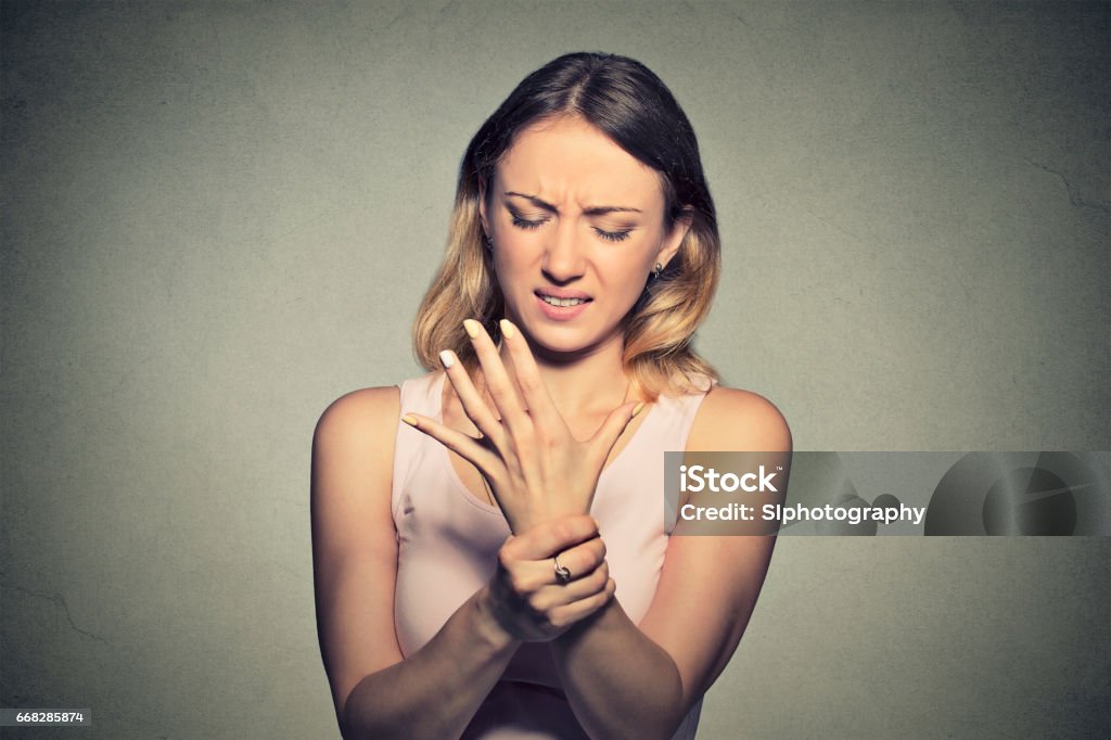 Young woman holding her painful wrist Young woman holding her painful wrist isolated on gray wall background. Sprain pain"n Carpal Tunnel Syndrome Stock Photo