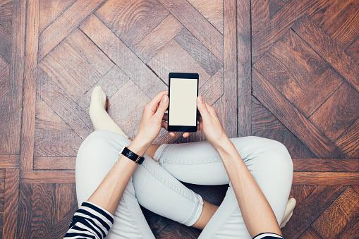 Girl in jeans sitting on the floor at home and using a mobile phone, a top view