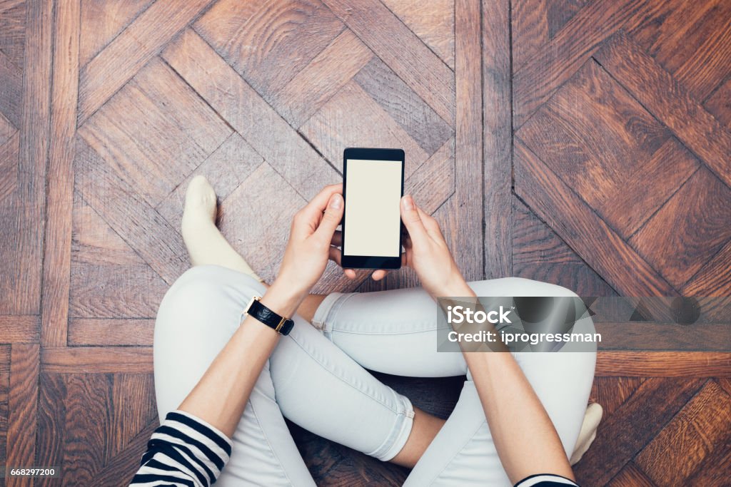 Girl in jeans sitting on the floor at home and using a mobile phone Girl in jeans sitting on the floor at home and using a mobile phone, a top view Mobile Phone Stock Photo