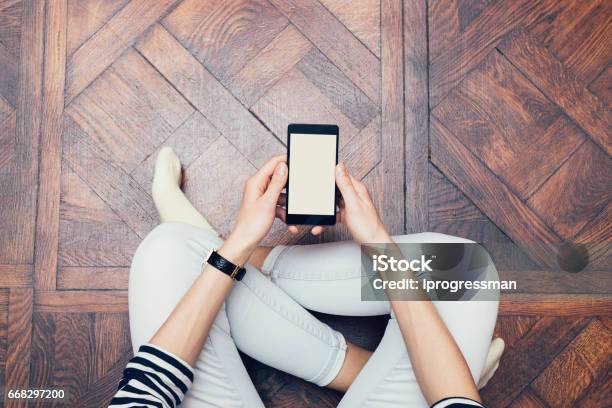 Girl In Jeans Sitting On The Floor At Home And Using A Mobile Phone Stock Photo - Download Image Now