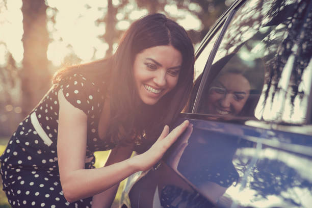 興奮して若い女性と屋外で背景に日当たりの良い森林の彼女の新しい車。 - car cleaning ストックフォトと画像