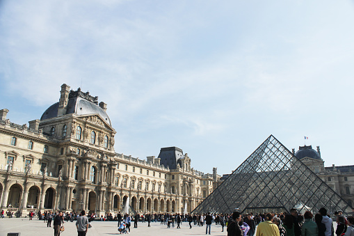 People milling around the Louvre Pyramid on a sunny day, Paris.