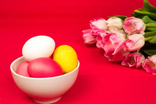 easter background, colorful eggs in ceramic bowl and roses bouquet over red paper