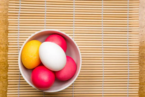 easter backdrop, colorful eggs in ceramic bowl on bamboo mat, top view