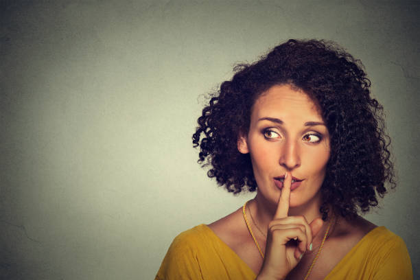 istock secretive young woman placing finger on lips asking shh 668354598