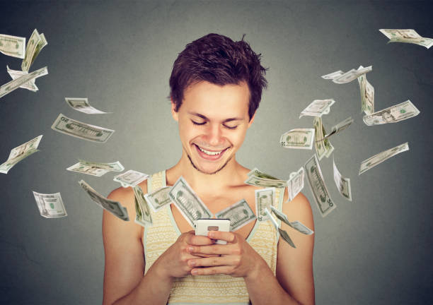 istock Happy young man using smartphone with dollar bills flying away from screen 668409350