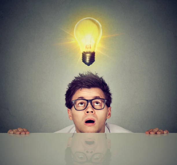 istock Man coming out from under the table looking up at bright light bulb above head 668410172