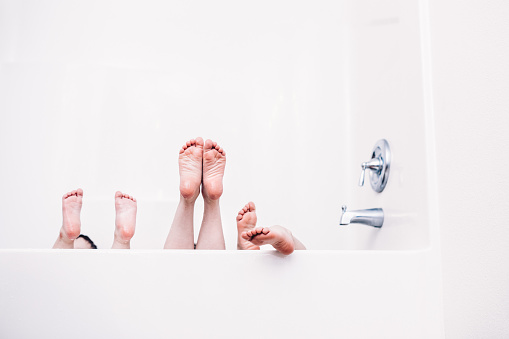 A fun image of siblings playing in the tub while taking a bath, their feet stick up out of the water into the air.  Horizontal image with copy space.