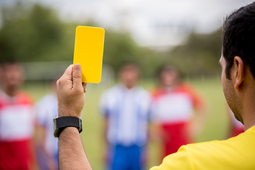 Close-up on the referee's hand showing a yellow card at a soccer game - sports concepts
