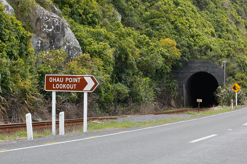 Photograph taken in the city of Kaikoura in New Zealand where a tunnel is seen on a mountain where the train passes and the car road to the side