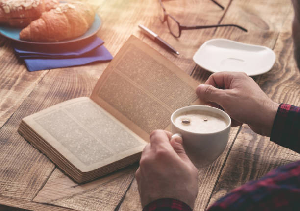 istock Man eating french breakfast and reading book while sitting at a wooden table 668515924