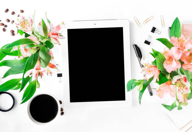 Workspace with tablet with blank screen, different office accessories, cup of coffee and bouquet of flowers. Flat lay, top view