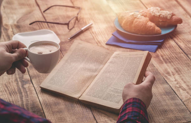 istock Man reading an old book and drinking coffee sitting at a wooden table 668515962