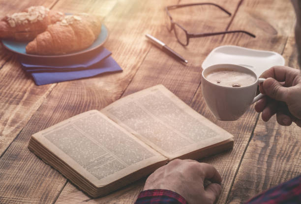 istock Man at home sitting at a wooden table relaxing reading book and drinking coffee 668515988