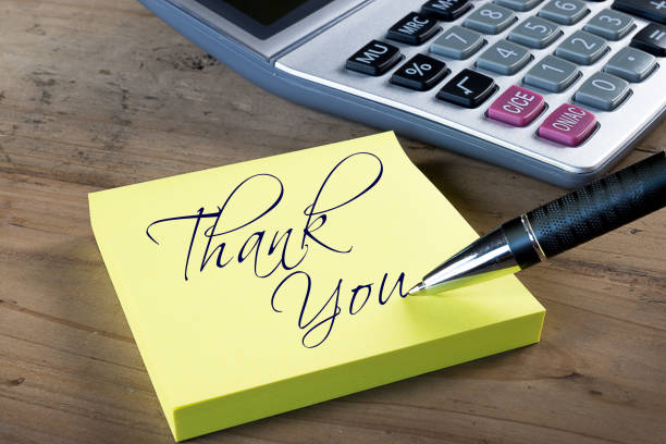 Yellow thank you note. Yellow sticky note with "Thank you" written with pen. Administrative Professionals or Secretaries day concept. Calculator in background. professional thank you stock pictures, royalty-free photos & images