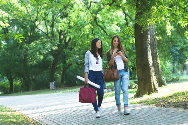 istock Two smiling female students walking in city park. 668560710