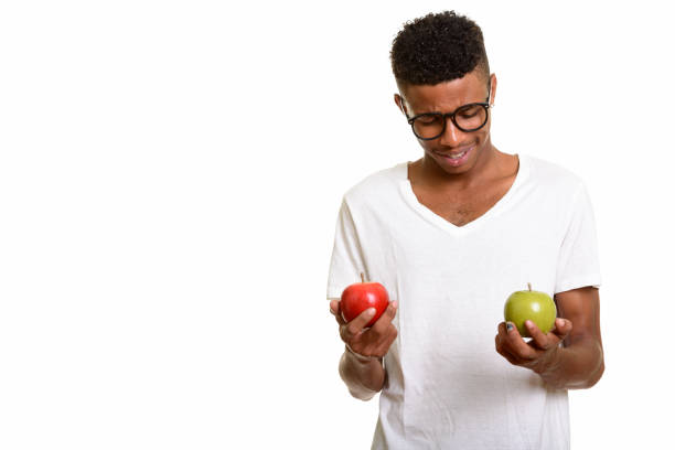 istock Young happy African man smiling while holding red apple and looking at green apple with eyeglasses 668562670