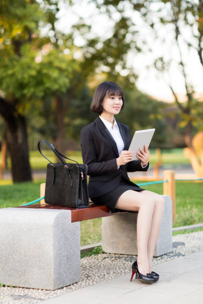 istock chinese female professional white-collar, sitting on a In the park bench, using her tablet computer 668571746