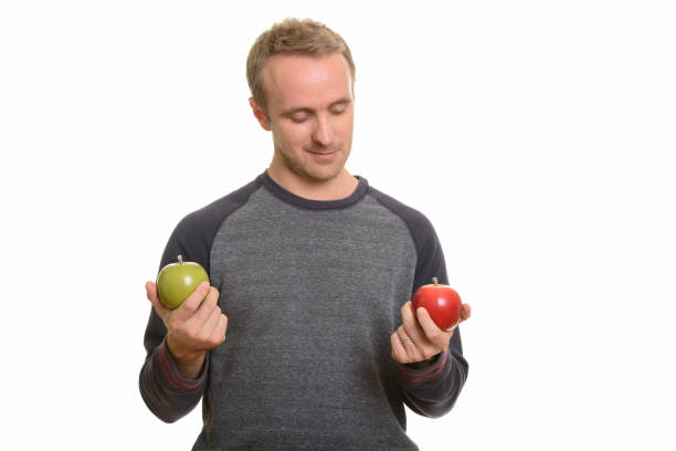 istock Handsome man looking at red apple and holding green apple 668572264