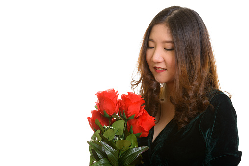 Close up of young happy Asian woman smiling while looking at red roses ready for Valentine's day horizontal shot