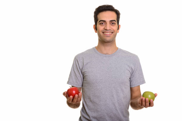 istock Young happy Persian man smiling while holding red apple and green apple ready for gym 668582362
