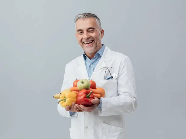 Smiling nutritionist holding fresh vegetables and fruit: healthcare and healthy vegetarian diet concept