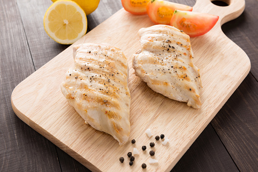 Marinated grilled chicken breasts on the wooden table.