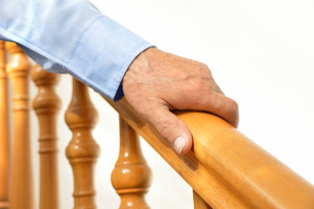 hand of senior man over a wooden railing closeup of senior man using the wooden railing of stairs to go downstairs at his home baluster stock pictures, royalty-free photos & images