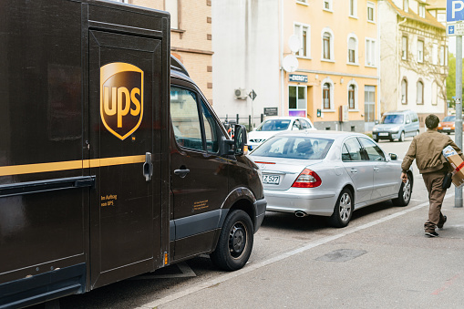 Kehl: UPS United Parcel Service worker leaving the brown van delivery UPS truck parked on a street to deliver the parcel to the client