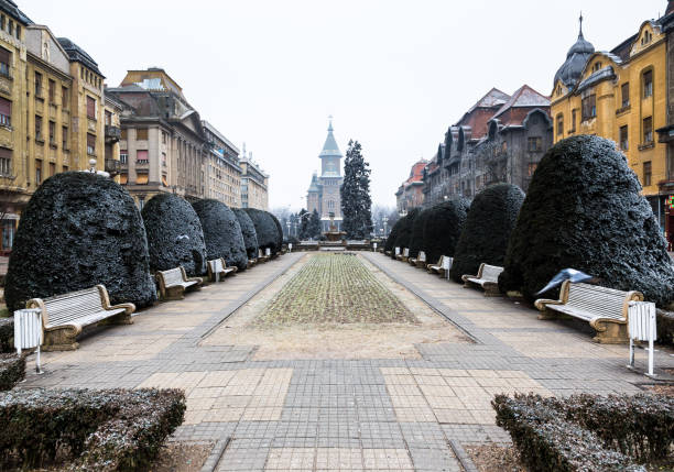 Winter scene outdoors in a public square central Timisoara, Romania. Frost covers the neatly trimmed hedges around the square, and the ground too. In the distance we can see one of the impressive orthodox cathedrals that the city - and Romania as a whole - is famous for. Horizontal colour wide angle image with copy space.