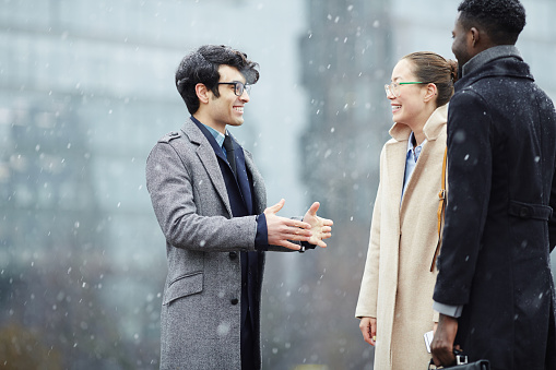 Multi-ethnic group of smiling business people meeting in snowy city street, smiling and talking, gesturing actively