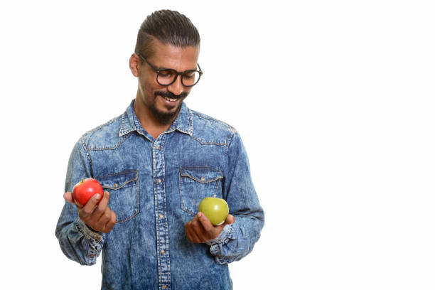 istock Young happy Indian man smiling while choosing between red and green apple 668603052