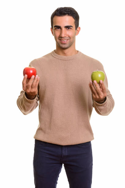 istock Young happy Persian man standing while holding red and green apple 668609820