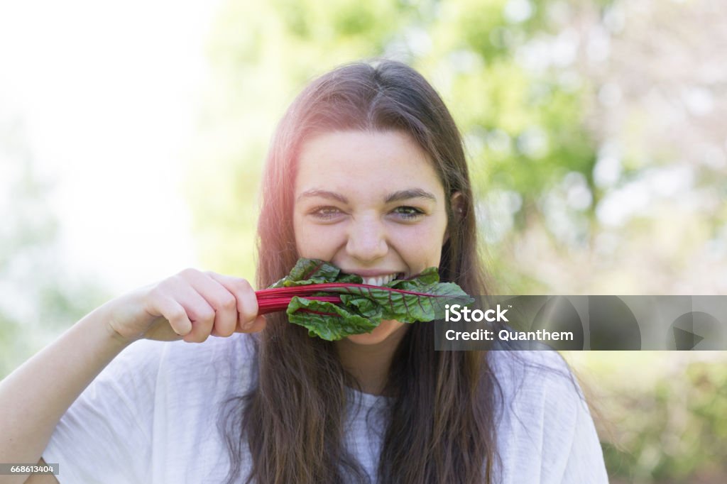 A girl biting a leaf of ruby red chard A girl biting a leaf of raw ruby red chard Vegetarian Food Stock Photo