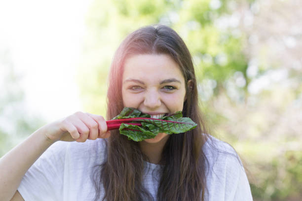 uma garota mordendo uma folha de acelga vermelha rubi - ruby red chard - fotografias e filmes do acervo