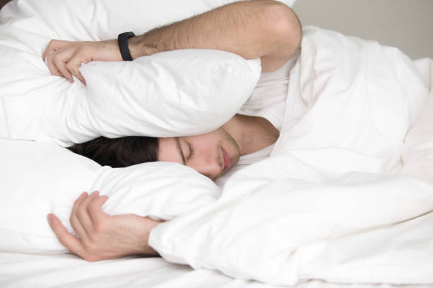 istock Young guy trying to sleep, covering his head with pillow 668624316