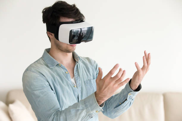 Man in virtual reality headset glasses looking at his hands Trying VR headset for the first time at home, young guy looking at his hands wearing virtual reality glasses, innovative future realistic technology for mobile apps and gaming head mounted display stock pictures, royalty-free photos & images