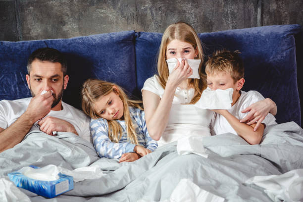 Sick family on bed Family of four has a flue and lying on bed together sneezeweed stock pictures, royalty-free photos & images