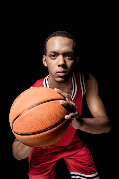 istock Young athletic man in uniform playing basketball on black 668638344