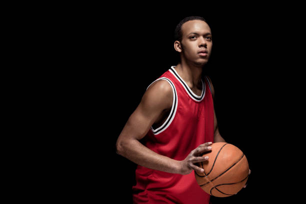 istock Young athletic man in uniform playing basketball on black 668638406