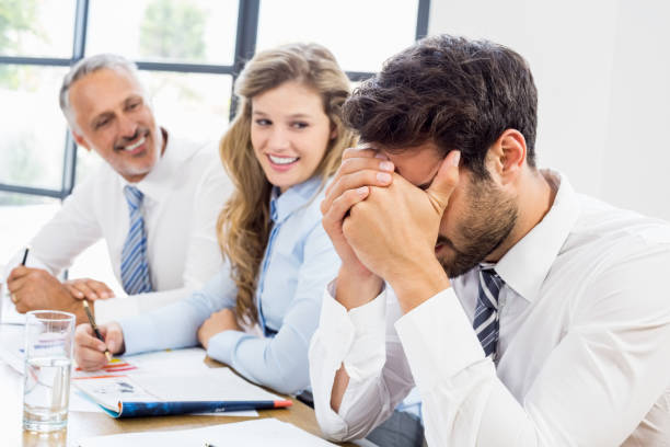 istock Smiling colleagues looking at frustrated businessman 668641126