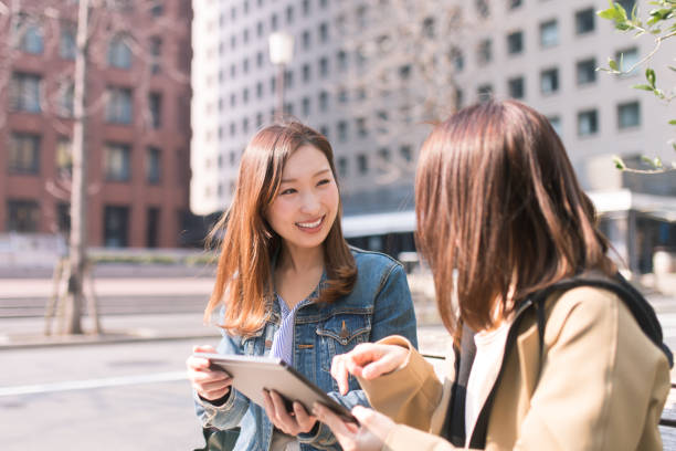 istock Young women talking in city, using digital tablet 668670874