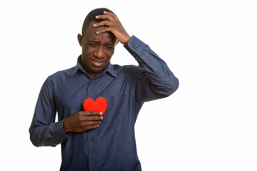 Sad African man crying while holding red heart on chest horizontal shot