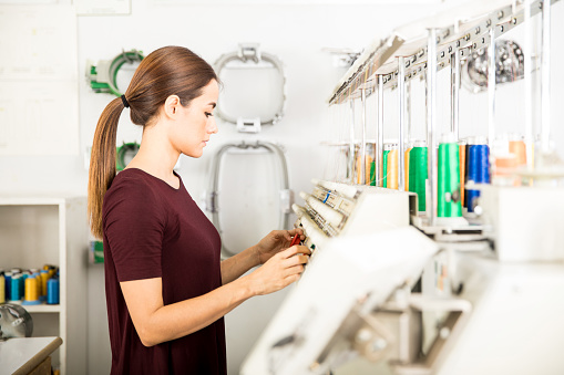 Profile view of a young woman setting up some threads in an embroidery machine in a textile factory